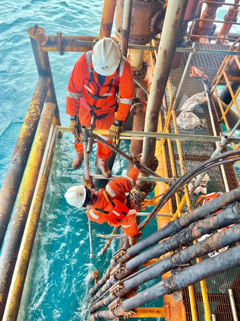 Pekerja konstruksi menggunakan Alat Pelindung Diri (APD) lengkap saat bekerja di atas perancah scaffolding.